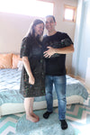 A mother and father smile while holding their newborn wrapped in a matching black paint-splatter swaddle. The mother wears a coordinating paint-splatter maternity robe, and the father wears a black “DAD” T-shirt included in the matching family hospital set. This paint splatter robe, dad shirt, and newborn swaddle bundle is ideal for maternity photos, labor and delivery outfits, hospital bag essentials, and baby announcement images.