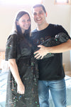 A mother and father smile while holding their newborn wrapped in a matching black paint-splatter swaddle. The mother wears a coordinating paint-splatter maternity robe, and the father wears a black “DAD” T-shirt included in the matching family hospital set. This paint splatter robe, dad shirt, and newborn swaddle bundle is ideal for maternity photos, labor and delivery outfits, hospital bag essentials, and baby announcement images.