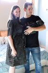 A mother and father smile while holding their newborn wrapped in a matching black paint-splatter swaddle. The mother wears a coordinating paint-splatter maternity robe, and the father wears a black “DAD” T-shirt included in the matching family hospital set. This paint splatter robe, dad shirt, and newborn swaddle bundle is ideal for maternity photos, labor and delivery outfits, hospital bag essentials, and baby announcement images.
