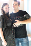 A mother and father smile while holding their newborn wrapped in a matching black paint-splatter swaddle. The mother wears a coordinating paint-splatter maternity robe, and the father wears a black “DAD” T-shirt included in the matching family hospital set. This paint splatter robe, dad shirt, and newborn swaddle bundle is ideal for maternity photos, labor and delivery outfits, hospital bag essentials, and baby announcement images.