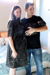 A mother and father smile while holding their newborn wrapped in a matching black paint-splatter swaddle. The mother wears a coordinating paint-splatter maternity robe, and the father wears a black “DAD” T-shirt included in the matching family hospital set. This paint splatter robe, dad shirt, and newborn swaddle bundle is ideal for maternity photos, labor and delivery outfits, hospital bag essentials, and baby announcement images.