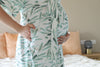 Person wearing a green leaf-patterned robe in a bedroom setting.