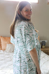 Woman wearing a green and white patterned dress standing in a bedroom.